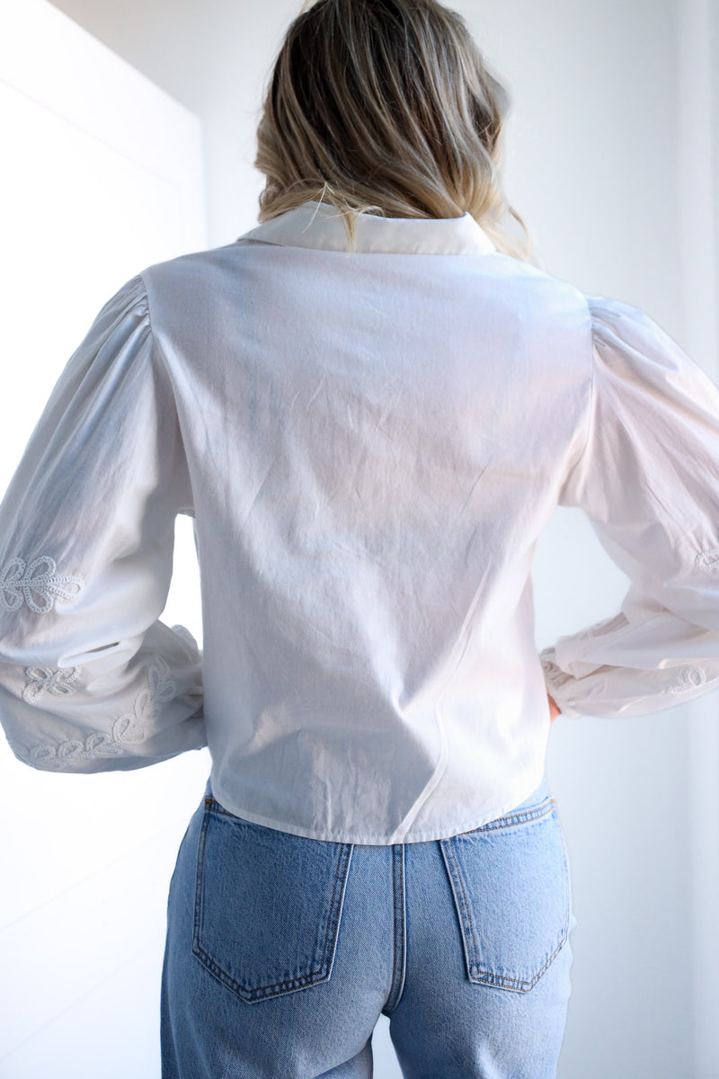 Person wearing a white blouse with lace details and blue jeans against a white background