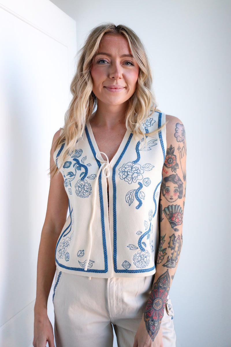 Woman wearing a white cardigan with blue floral patterns against a plain background