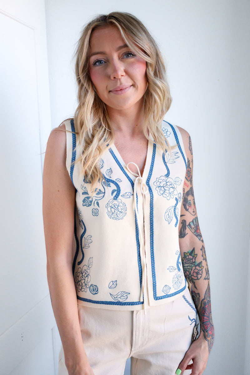 Woman wearing a sleeveless embroidered top against a white background