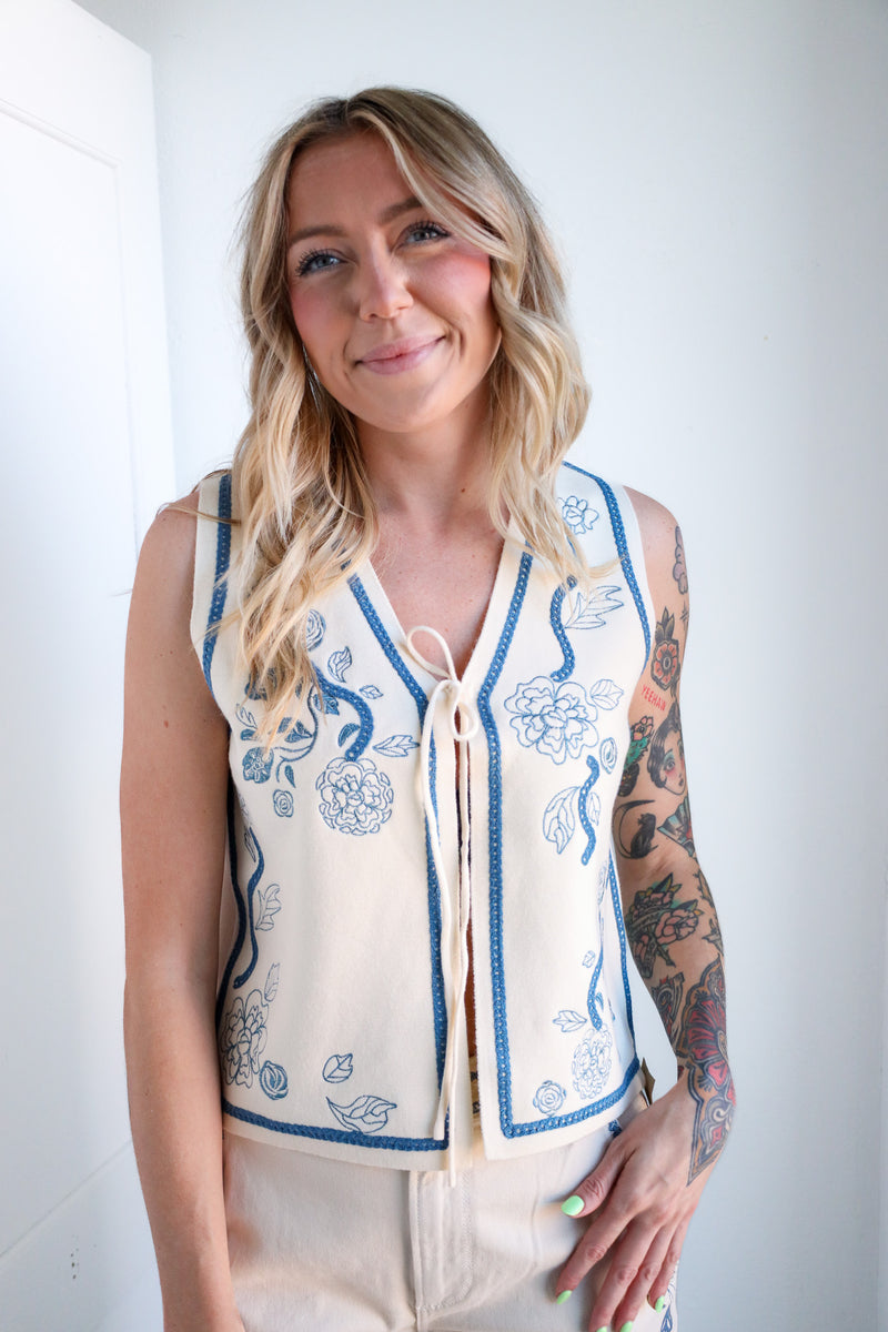 Woman wearing a sleeveless embroidered top against a white background