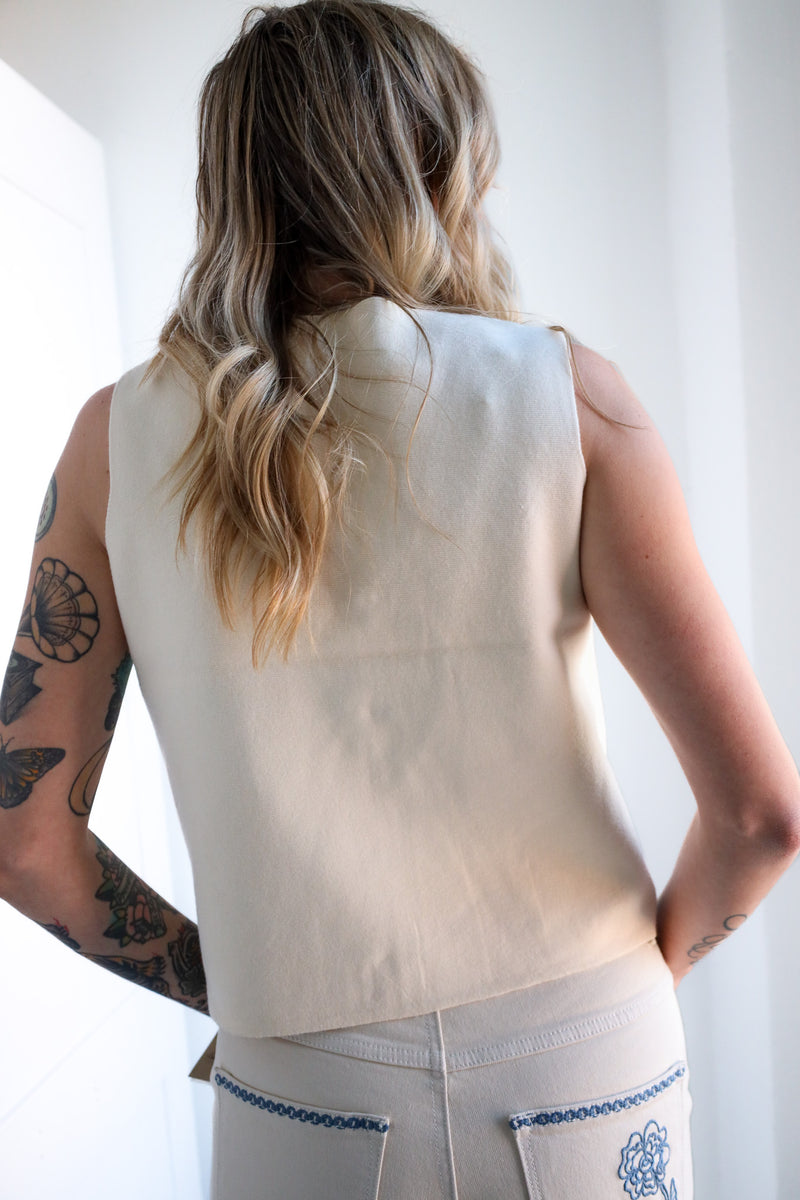 Person wearing a beige sleeveless top with a plain background