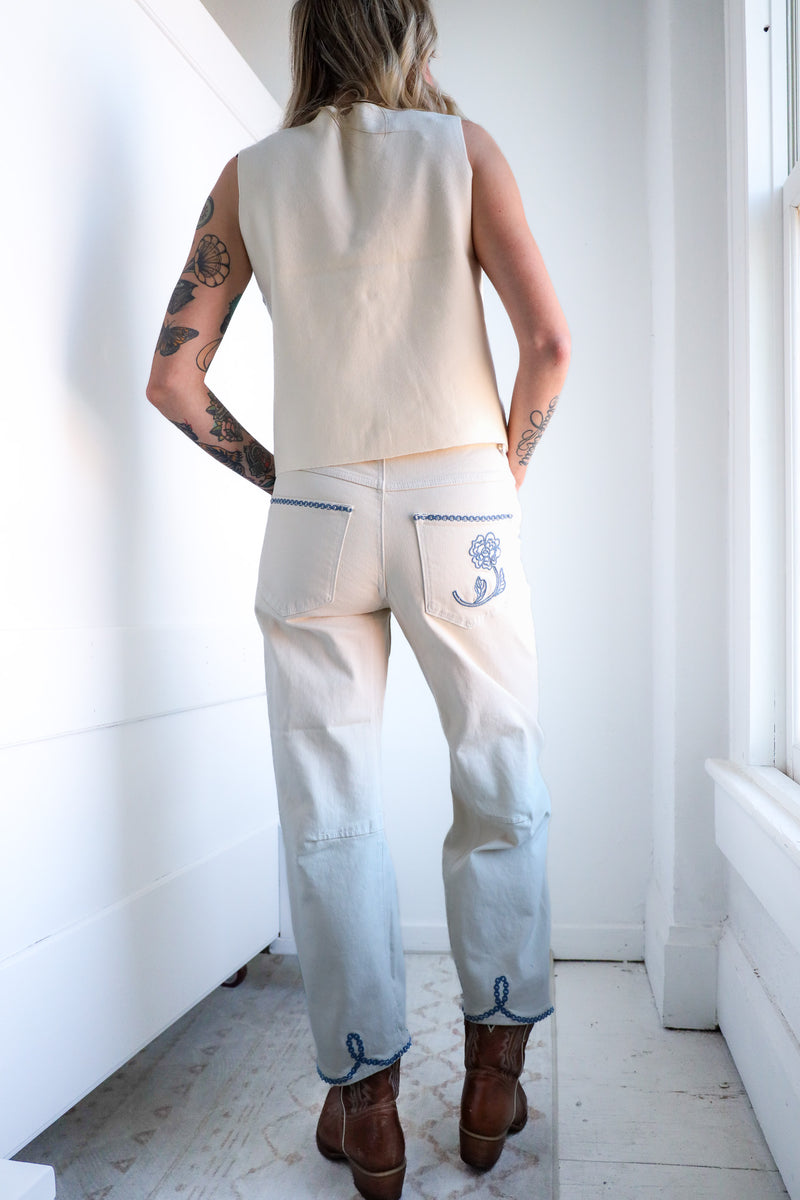 Person wearing a sleeveless top and light-colored pants with embroidery in a minimal indoor setting.
