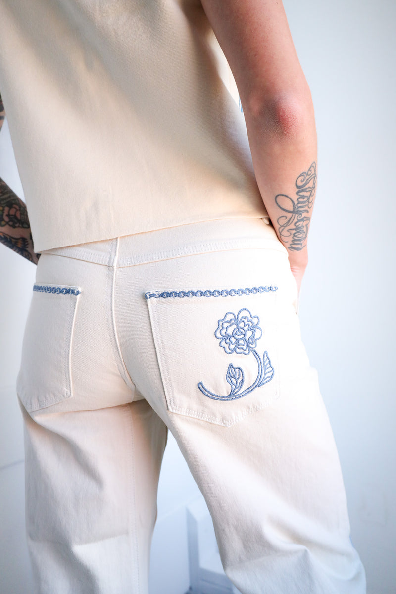 White pants with blue floral embroidery on a plain background