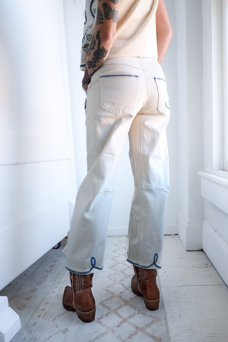 Person wearing white pants with blue hems and brown boots in a bright room.