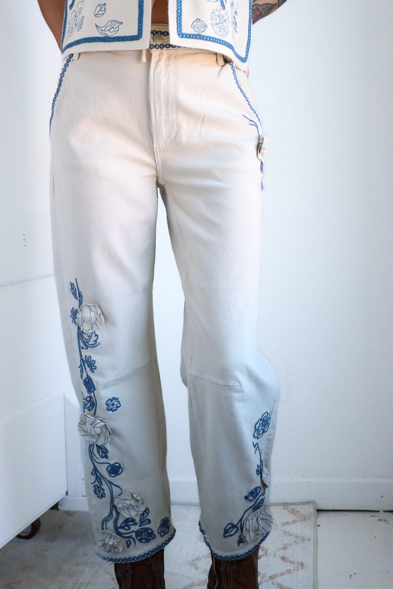 White pants with blue floral embroidery worn by a person against a white background