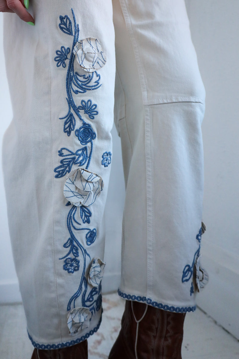 White pants with blue floral embroidery on a white background