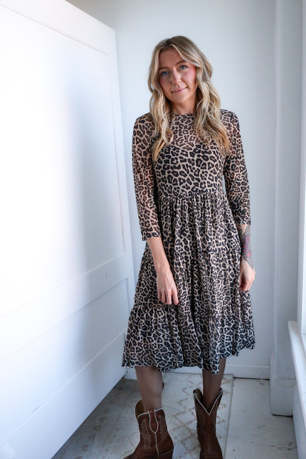 Woman wearing a leopard print dress with long sleeves in a minimalistic room.