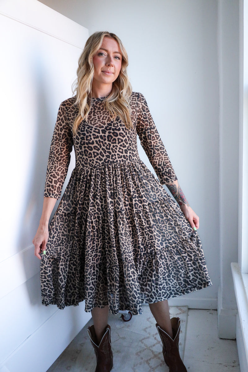 Woman wearing a leopard print dress standing against a white wall.