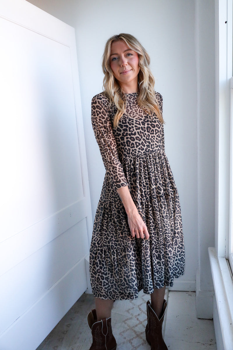 Woman wearing a leopard print dress standing against a white wall.
