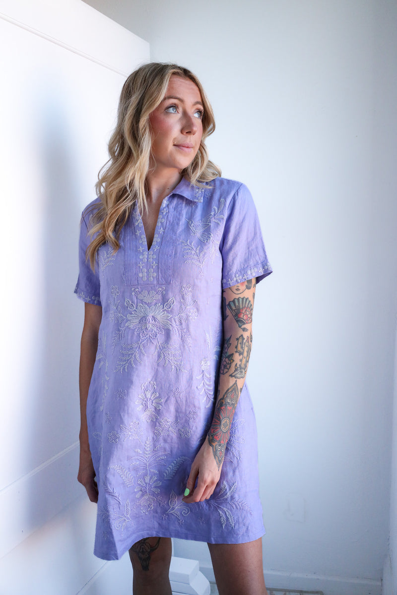 Woman wearing a purple dress with white patterns against a plain background