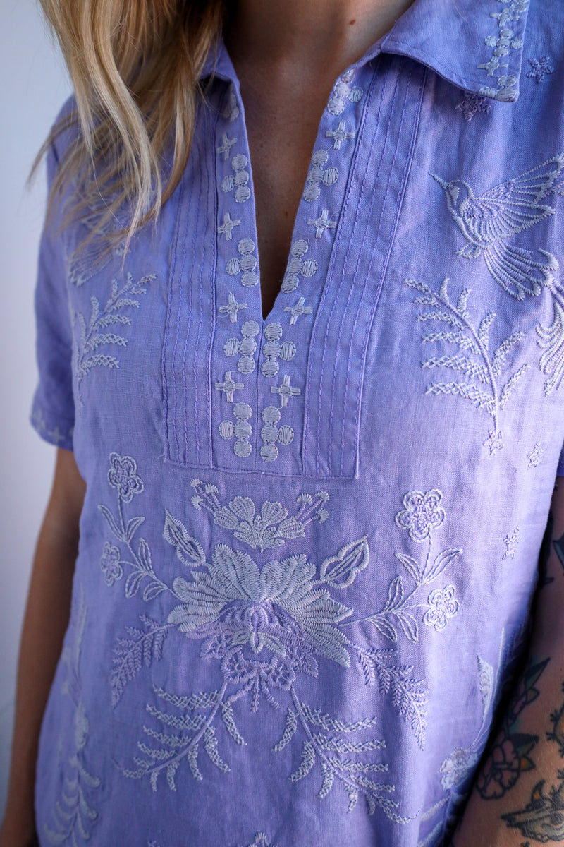 Close-up of a person wearing a light purple embroidered shirt with floral patterns.
