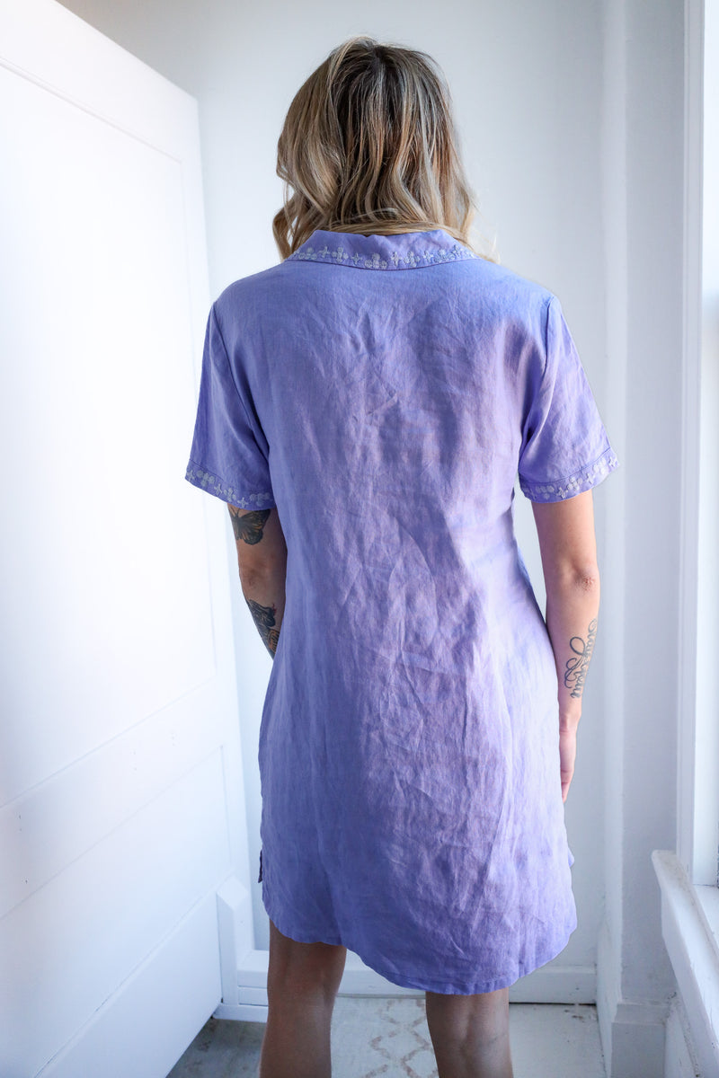 Person wearing a light purple dress standing in a room with white walls.