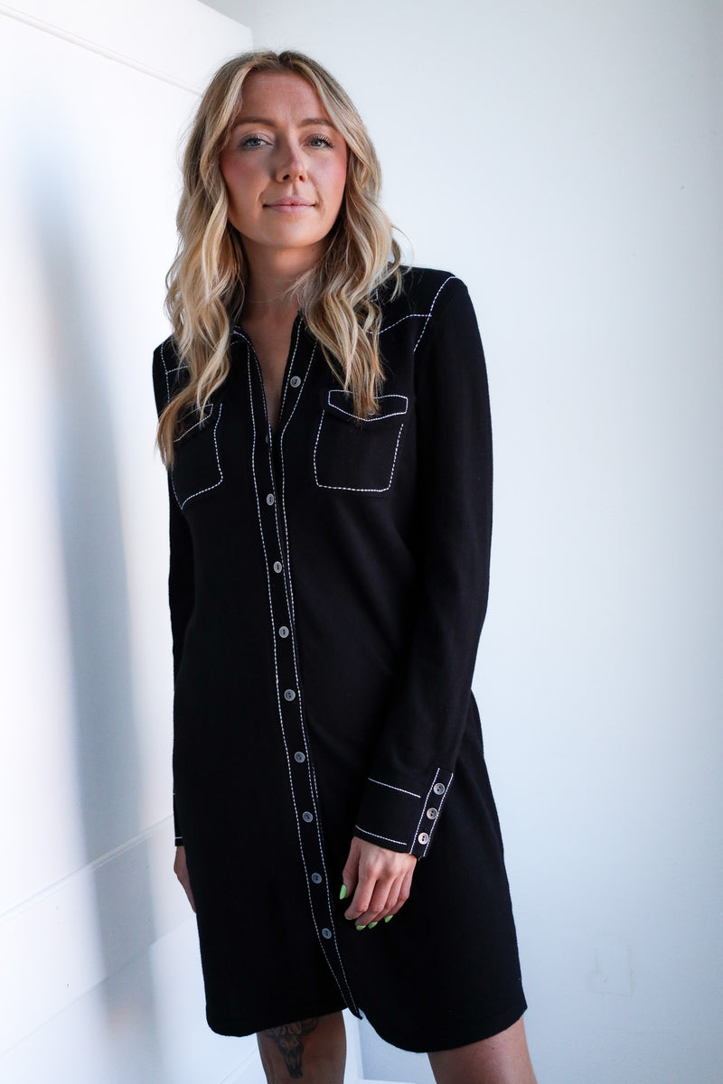 Woman wearing a black dress with white accents against a plain background
