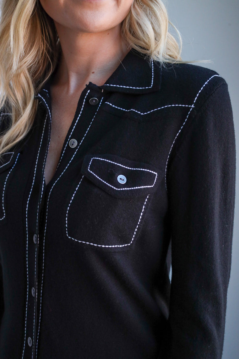 Black shirt with white stitching worn by a person against a gray background