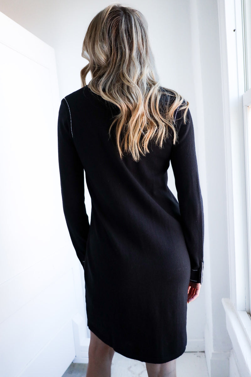 Person wearing a black dress standing in a bright room with white walls.