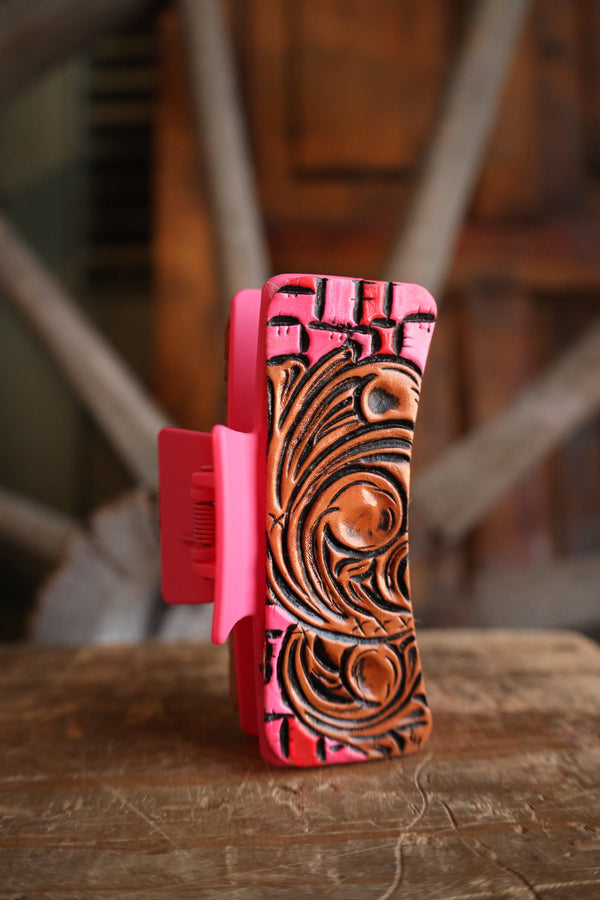 Pink claw clip with brown embossed design on a wooden surface