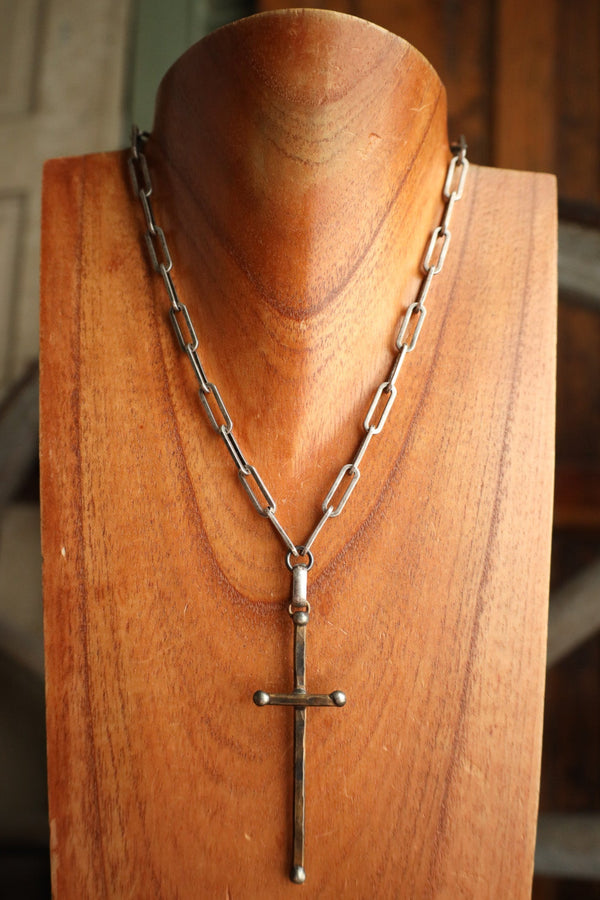 Silver chain necklace with a cross pendant on a wooden mannequin head.
