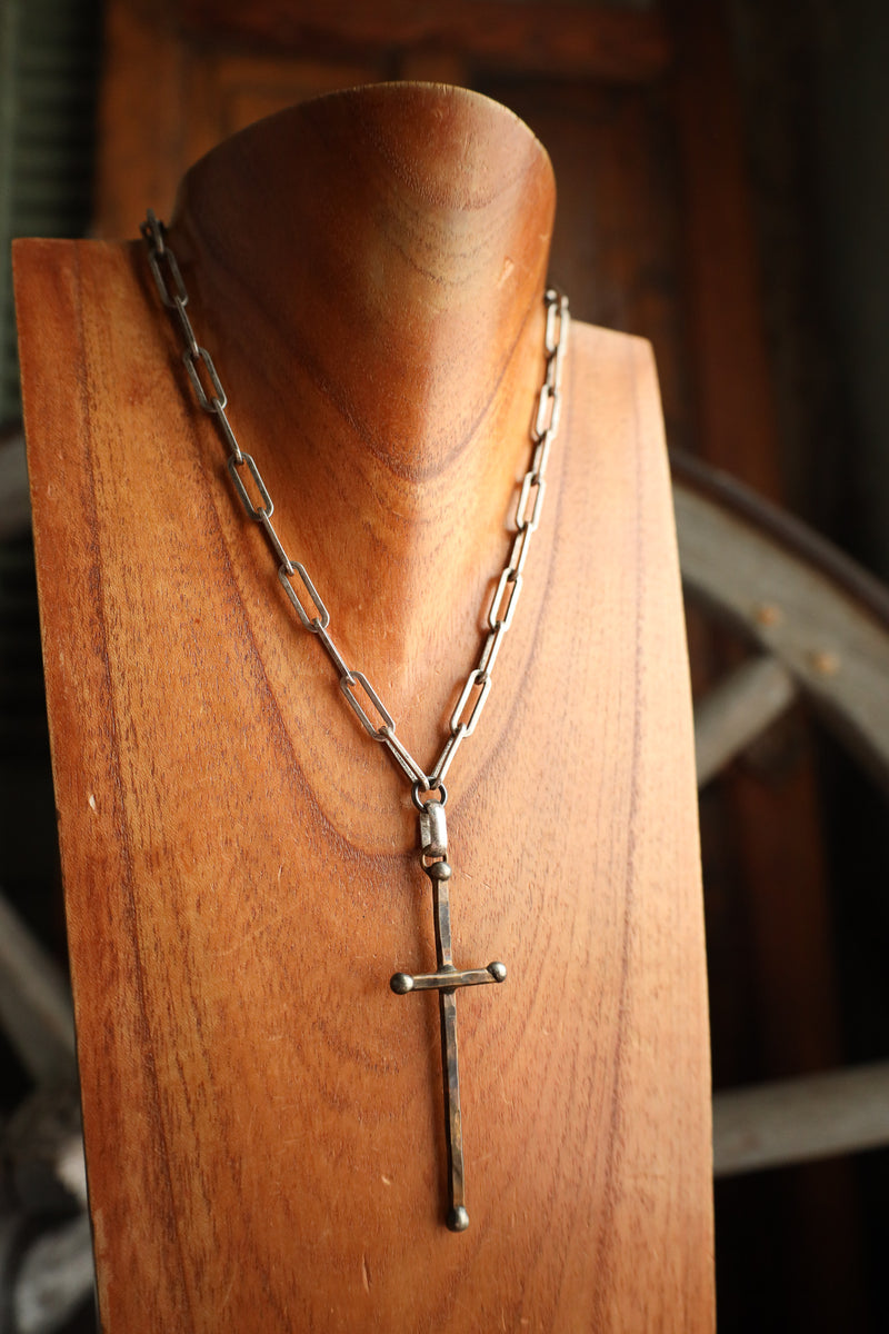 Silver chain necklace with a cross pendant on a wooden stand.