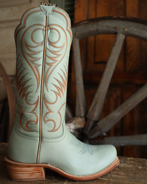 Light blue cowboy boot with intricate brown stitching on a wooden surface.