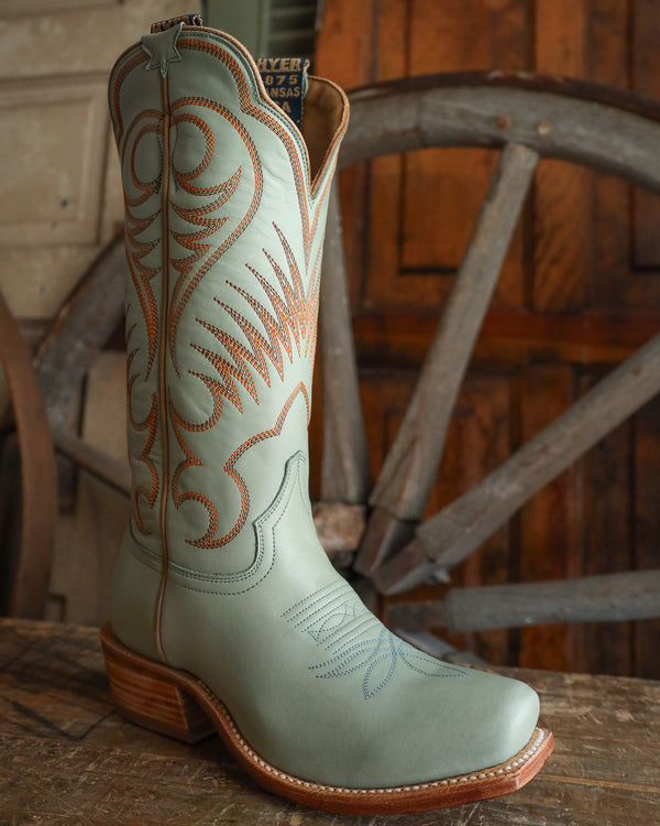 Light blue cowboy boot with brown stitching on a wooden surface
