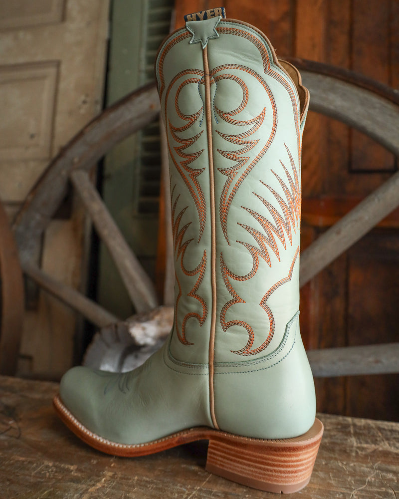 Light blue cowboy boot with brown stitching on a wooden surface