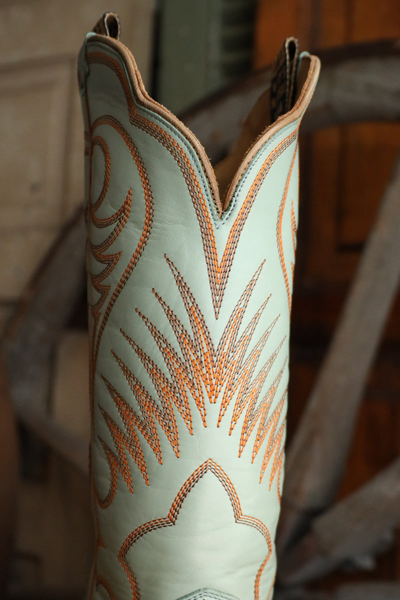 Close-up of a light blue cowboy boot with brown stitching on a blurred background
