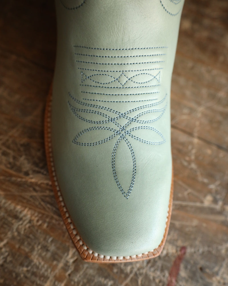Light green boot with floral embroidery on a wooden surface