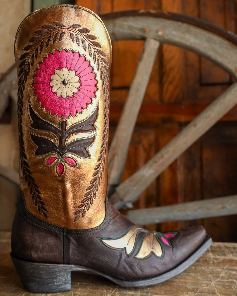 Brown cowboy boot with pink floral design against a wooden background