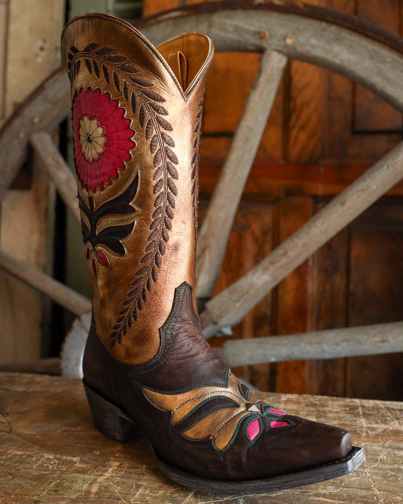 Decorative cowboy boot with floral patterns on a wooden surface and wheel background