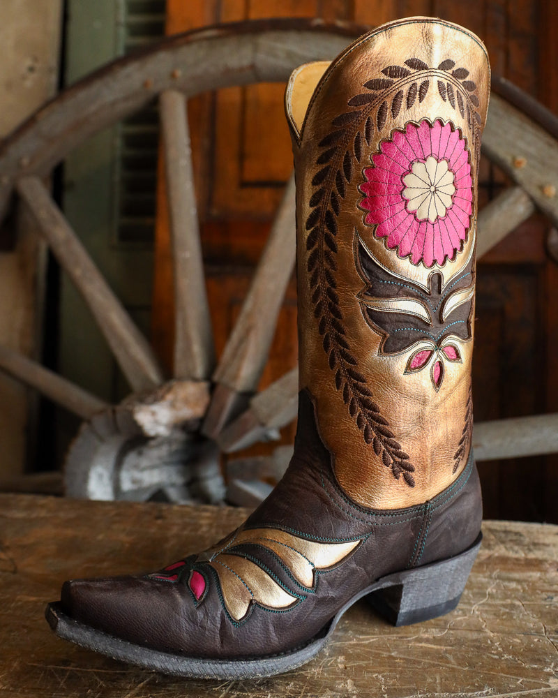 Decorative cowboy boot with floral design in front of a wooden wagon wheel.