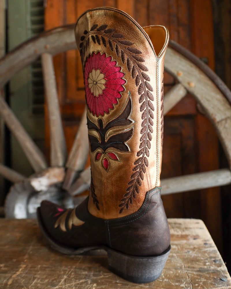 Brown cowboy boot with floral embroidery on a wooden surface with a wagon wheel in the background