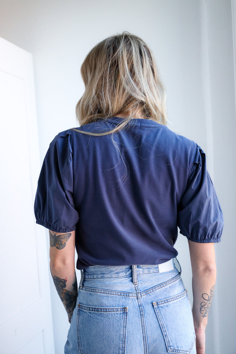 Person wearing a blue blouse and light blue jeans against a white wall