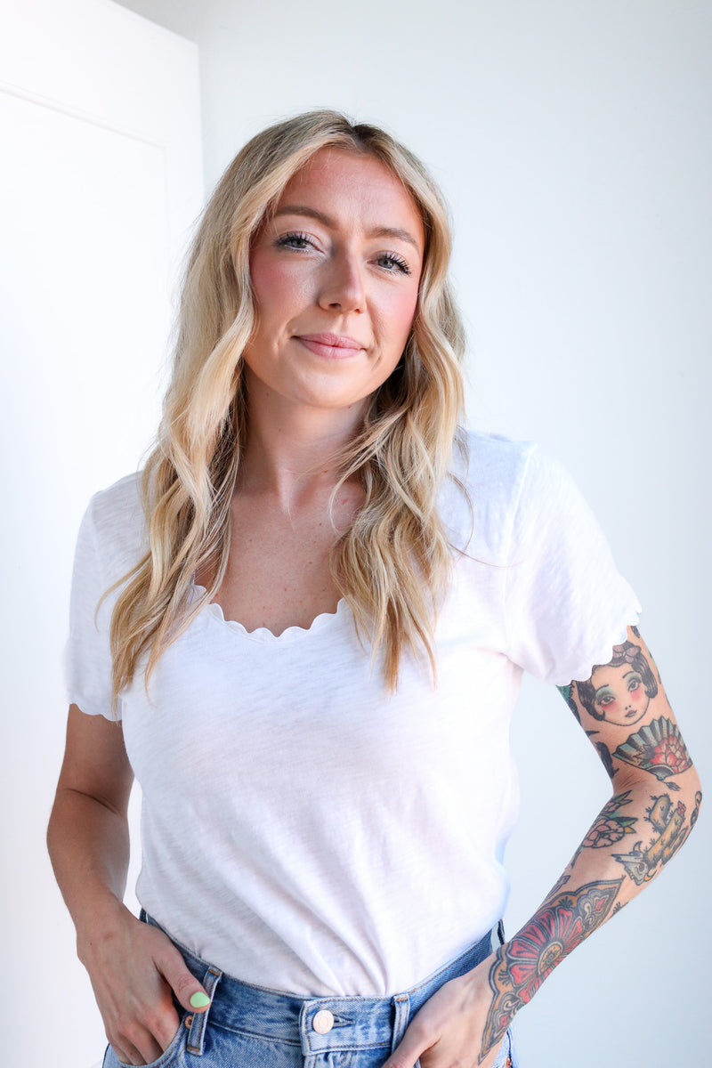 Woman wearing a white top and denim shorts with tattoos on her arms against a white background