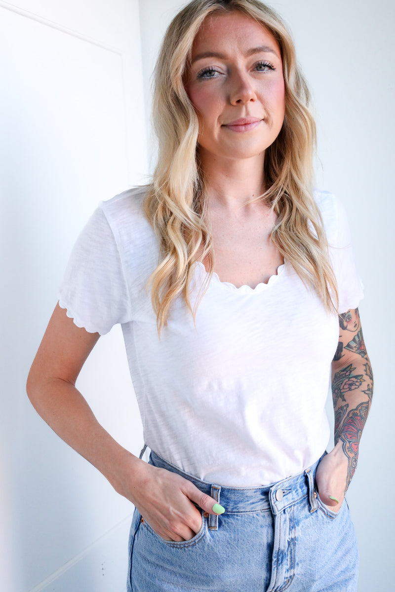 Woman wearing a white top and blue jeans against a plain background