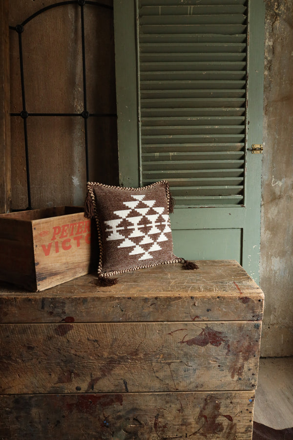 Brown square pillow with cream Aztec design on front with tassels on the corners