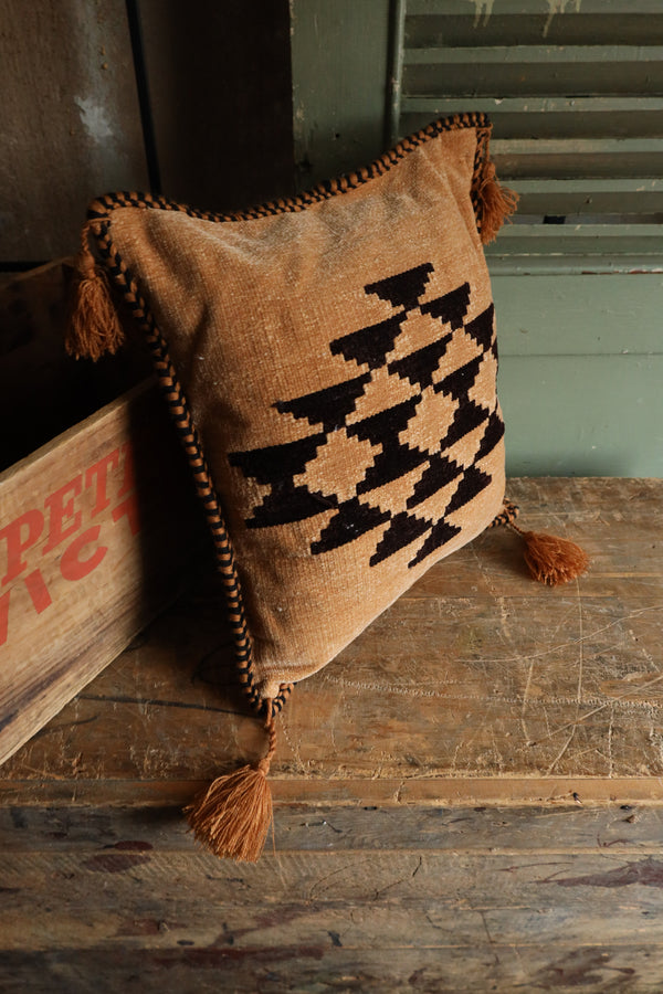 Square pillow with chocolate Aztec print on tan background pillow with tassels on corners.