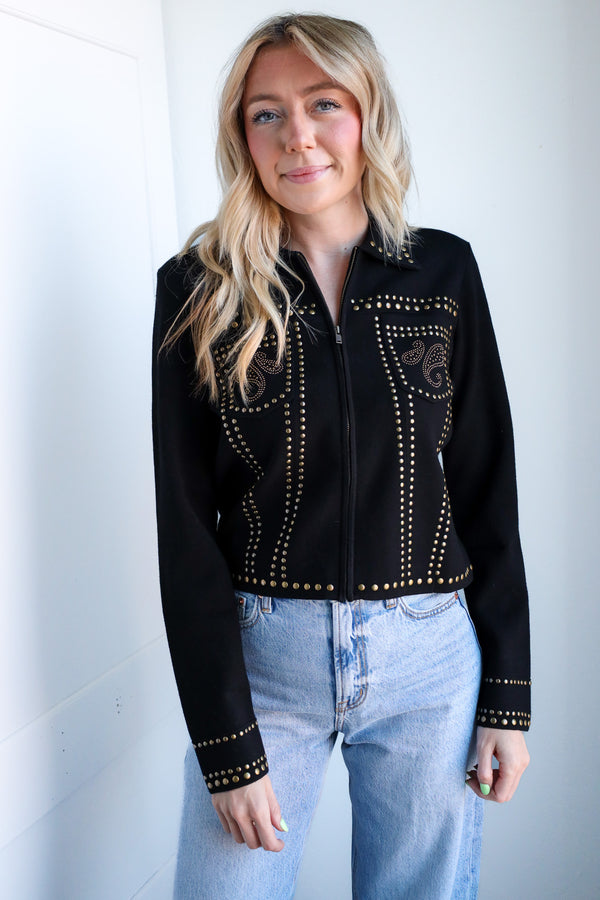 Woman wearing a black studded jacket and blue jeans against a white background
