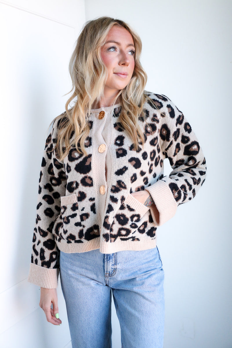 Woman wearing a leopard print cardigan and light blue jeans against a white background