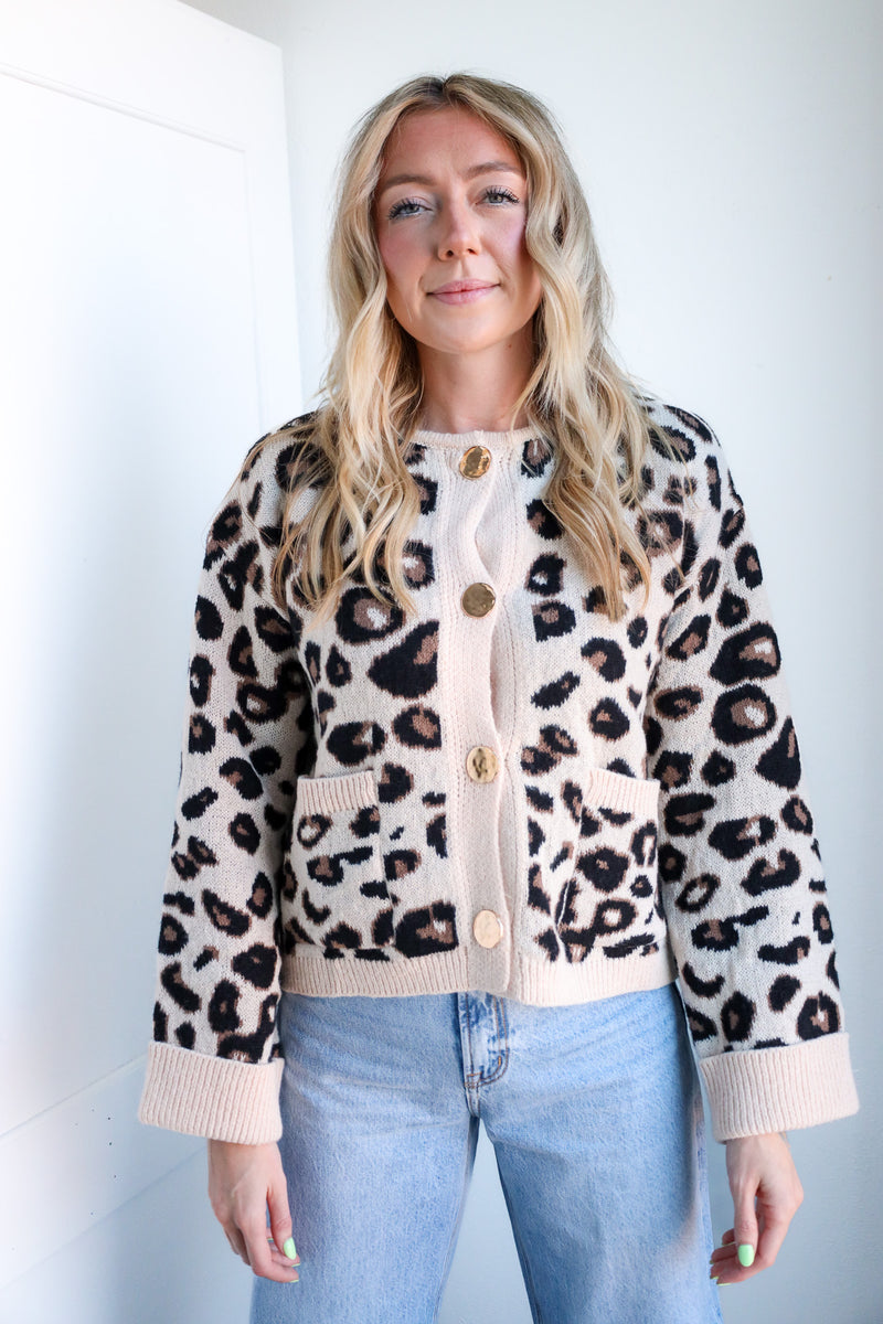 Woman wearing a leopard print cardigan with beige buttons against a white background