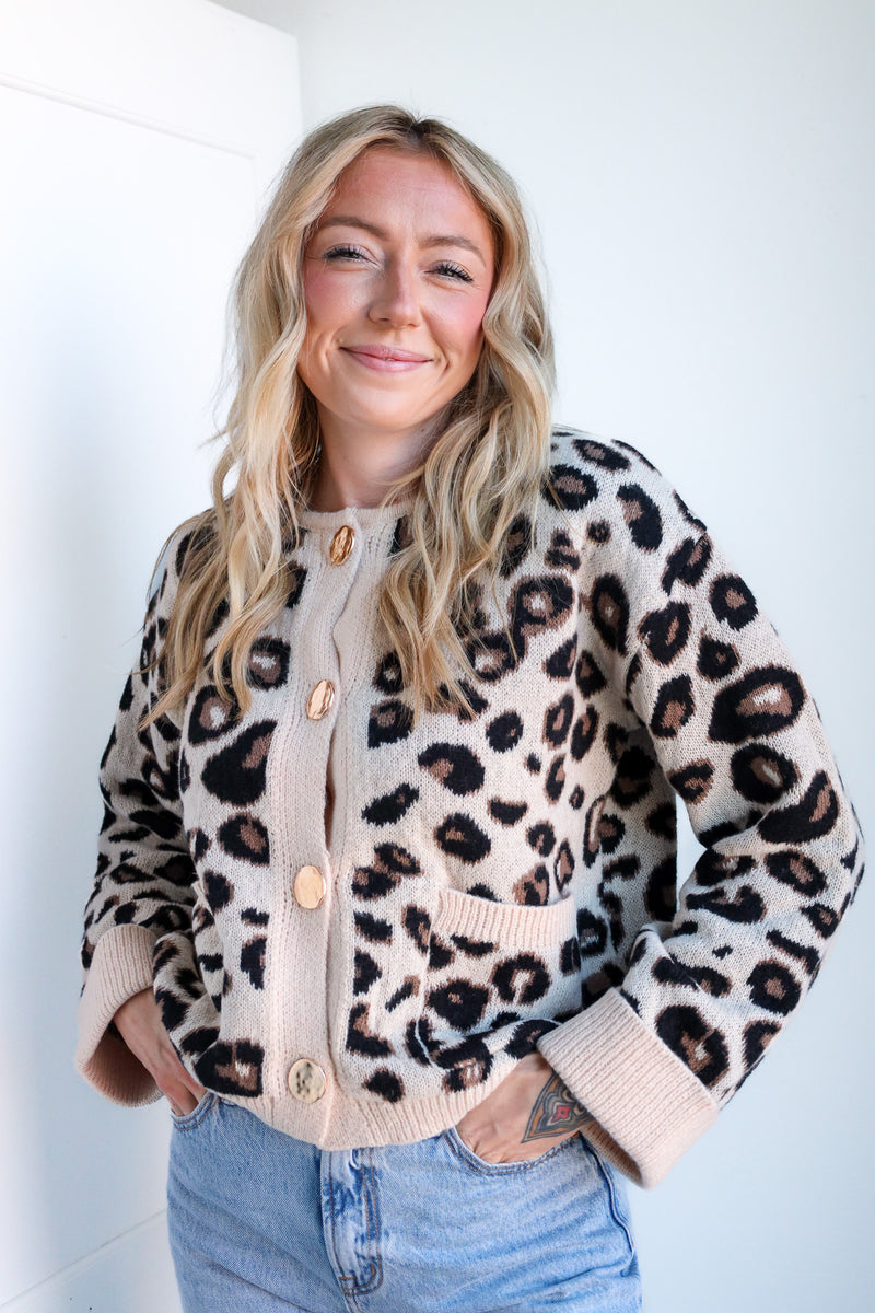 Woman wearing a leopard print cardigan with beige buttons against a white background