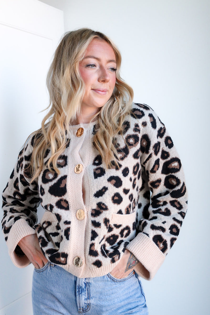 Woman wearing a leopard print cardigan with beige buttons against a white background