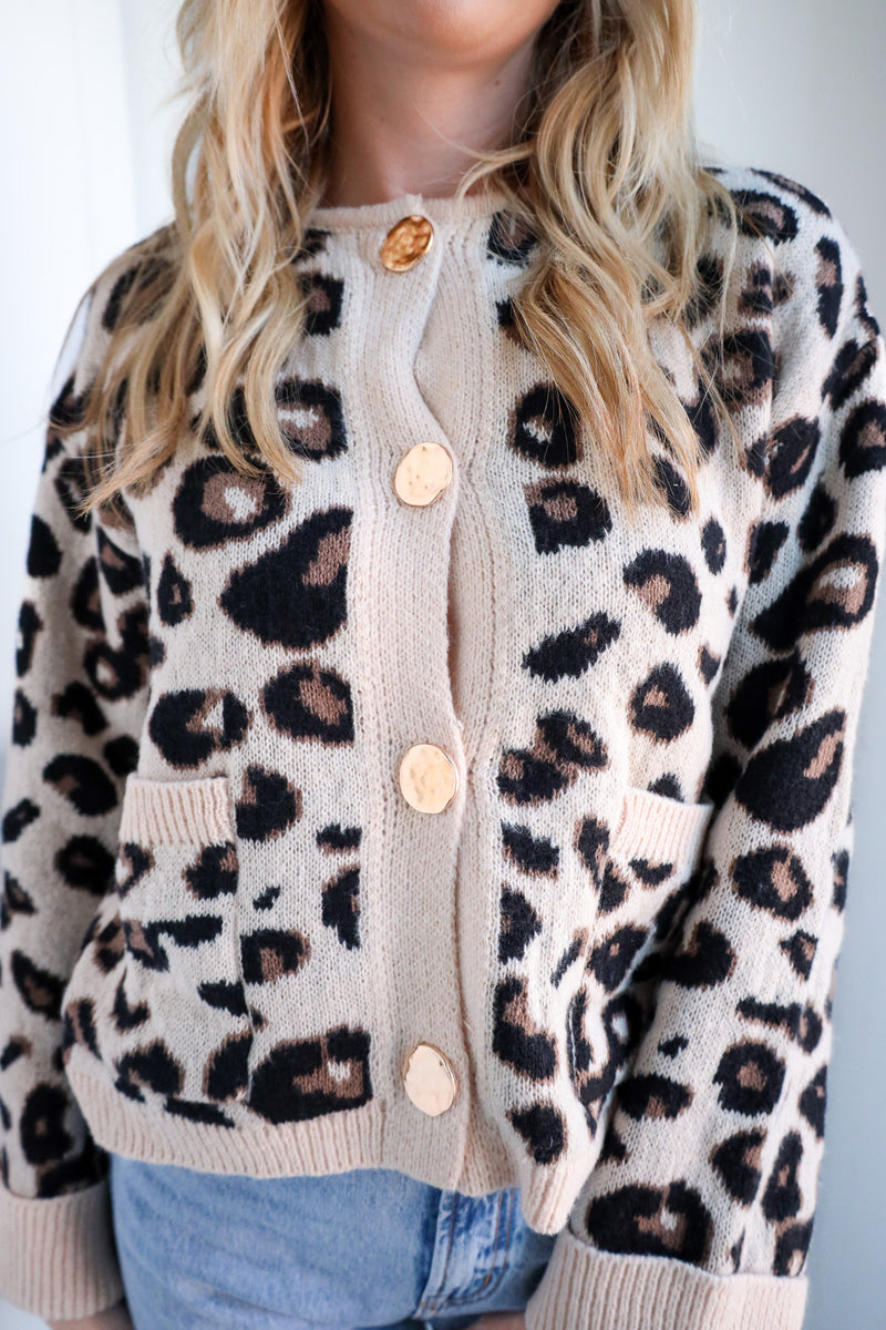 Person wearing a leopard print cardigan with beige buttons against a white background