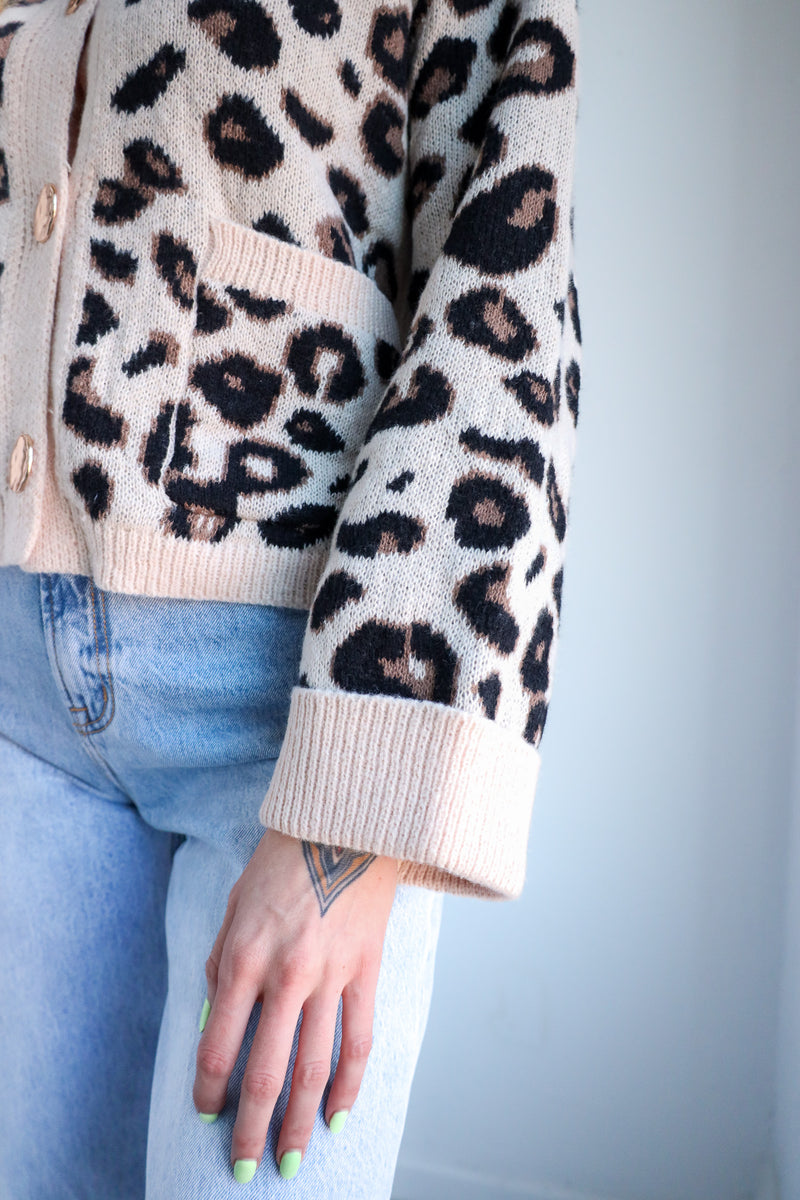 Leopard print sweater with beige cuffs and trim worn by a person against a light blue background