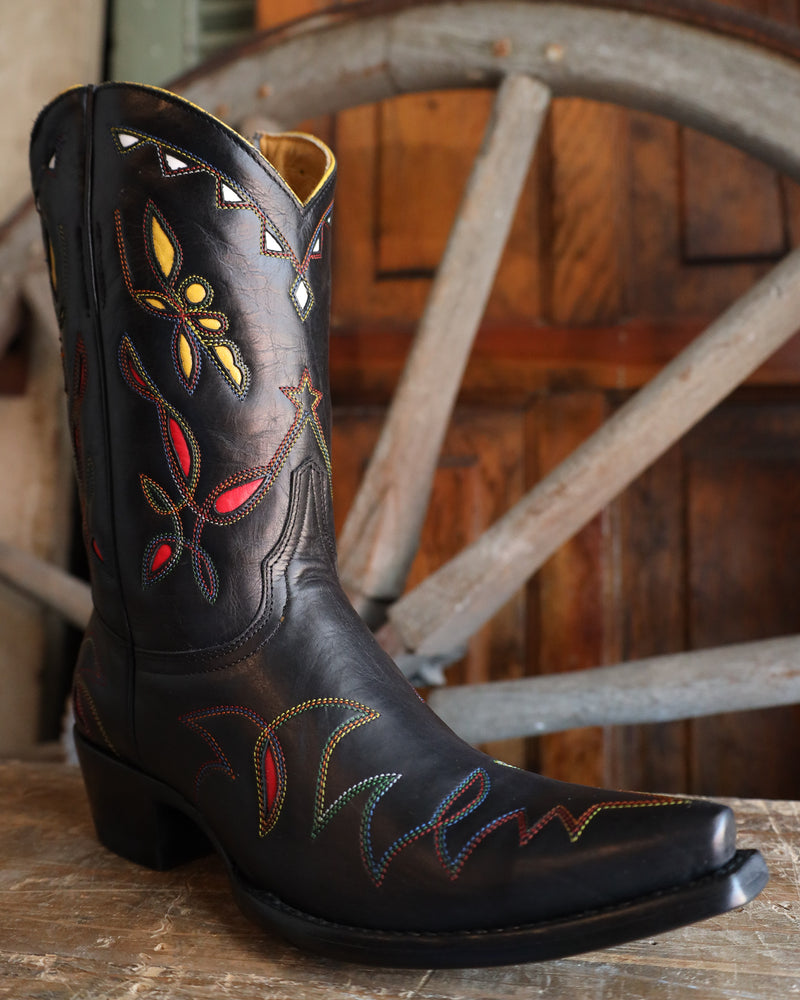 Black cowboy boot with colorful embroidery on a wooden surface with a rustic background