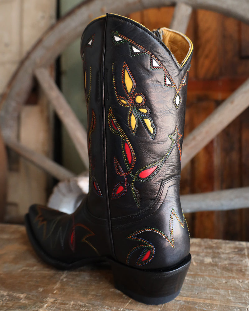Black cowboy boot with colorful embroidery on a wooden surface with a wheel in the background