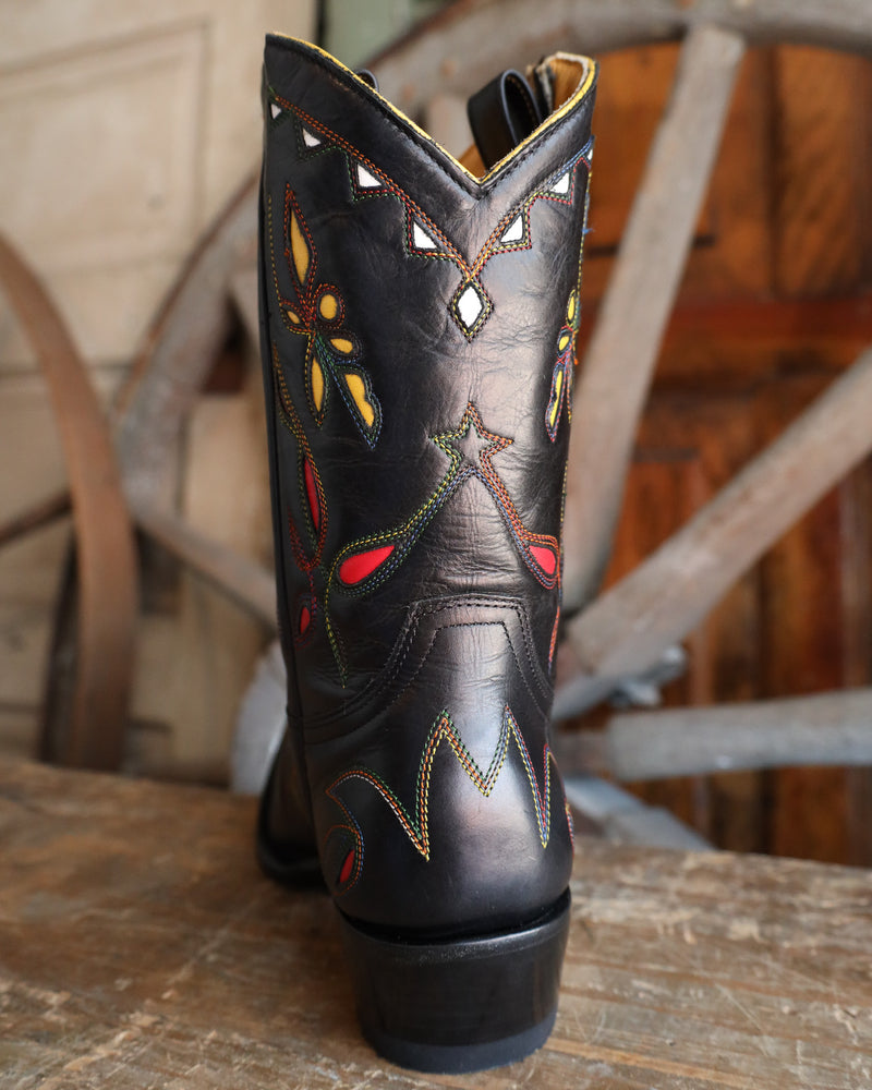 Black embroidered cowboy boot on a wooden surface with a rustic background