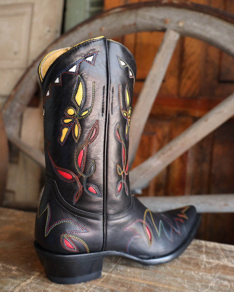Black cowboy boot with colorful embroidery on a wooden surface and background.