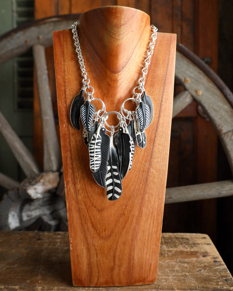 Necklace with feather charms on a wooden stand in front of a rustic background