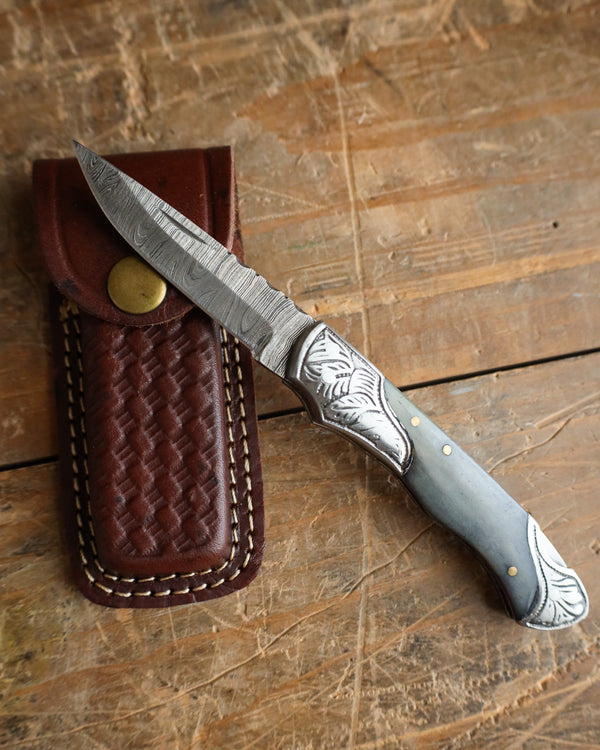 Knife with decorative handle and leather sheath on a wooden surface