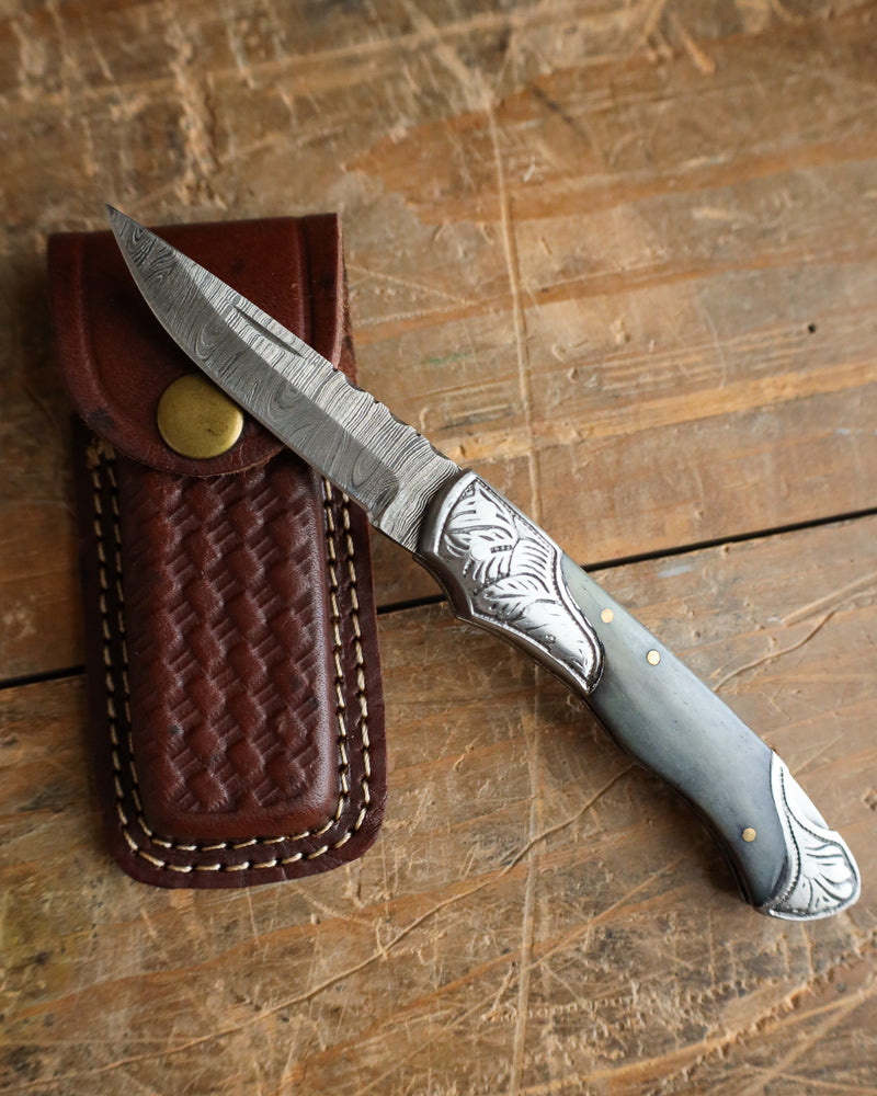 Knife with decorative handle and leather sheath on a wooden surface